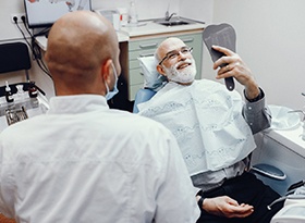 A man smiling at himself in the mirror at the dentist office