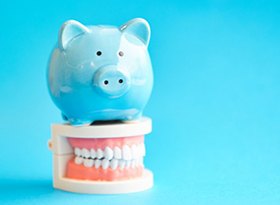 piggy bank on top of false teeth against light blue background 