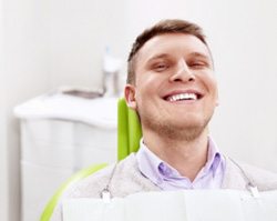 Man in grey sweater smiling while relaxing in dental chair